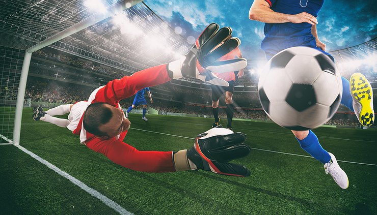 Footballer in Blue Scoring Past Diving Goalkeeper
